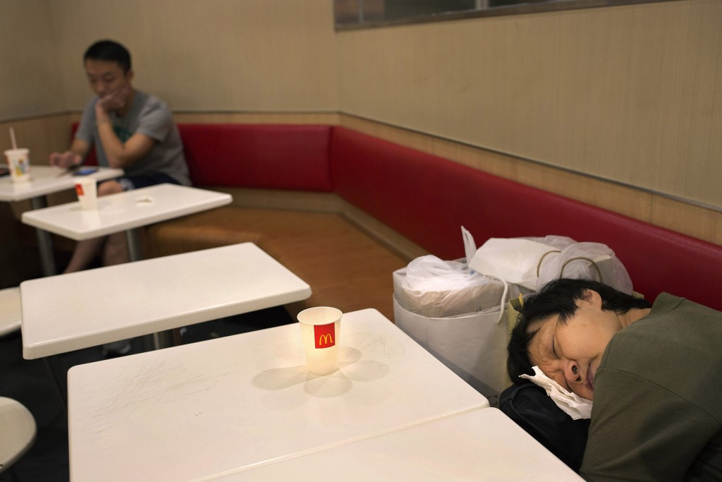 In this Oct. 30, 2015 photo, a woman sleeps with her belongings at night in a 24-hour McDonald’s branch in Hong Kong. The recent death of a woman at a Hong Kong McDonald’s, where her body lay slumped at a table for hours unnoticed by other diners, has focused attention on the city’s “McRefugees” down and out people who spend their nights the fast food outlet’s 24-hour branches because they’ve nowhere anywhere else to go. (AP Photo/Vincent Yu)